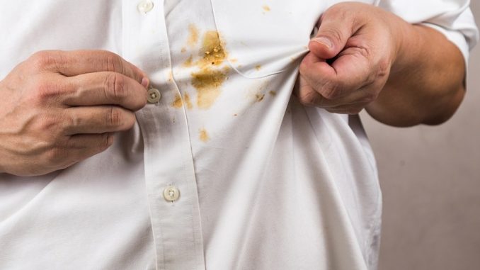 Person pointing to spilled curry stain on white shirt.
